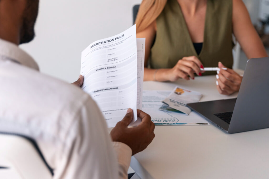 A close-up of a man reviewing a registration form during a meeting with a professional woman at a desk, symbolizing job application processes and fair hiring practices like Ban the Box.